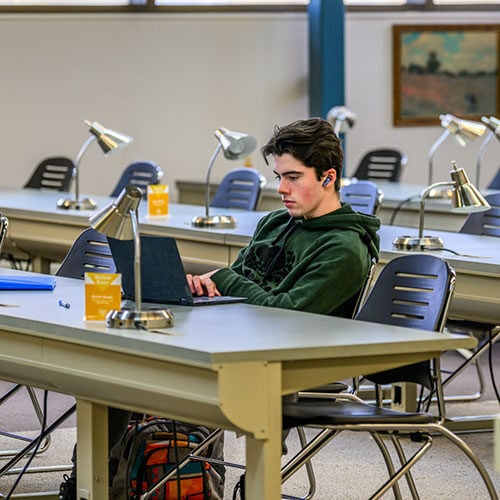 Male student studying on a laptop in the library