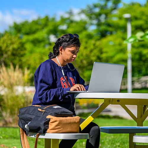 Female student studying on a laptop outside at a table